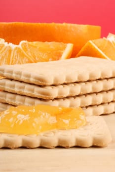 Biscuits, marmalade and slices of orange on a wooden cutting board.