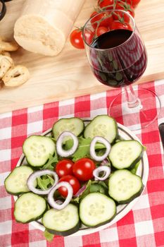 Close-up of a prepared table with an healthy salad, a glass of red wine, fork and knife. In the background some red tomatoes and parmesan cheese. Selective focus.