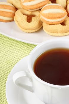 Close-up of a cup of tea and some shortcrust pastry biscuits over a light green background