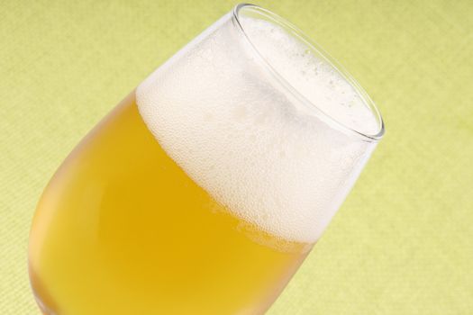 Close-up of a glass of cold pale lager beer over a light green background.