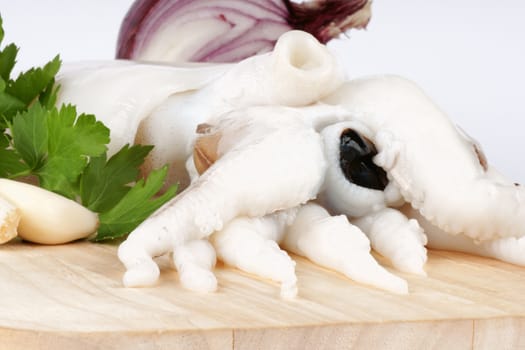 Raw cuttlefish on a wooden cutting board with red onion, parsley and garlic.