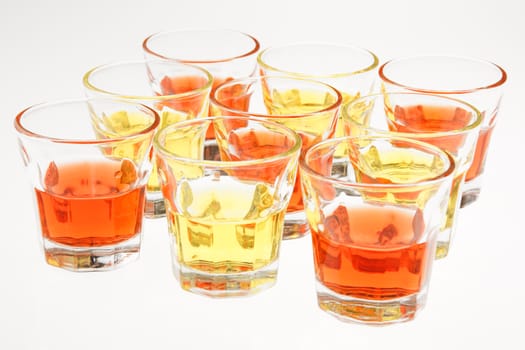 Close-up of some orange and yellow drinks served in mini glasses over a white background