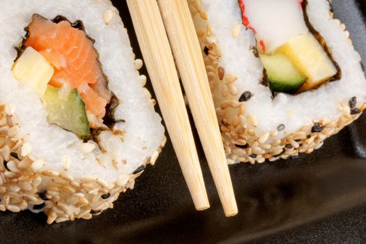 Macro of two sushi rolls with chopsticks over a black plate. Shallow DOF