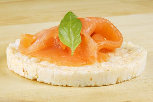 Close-up of a rice cake with smoked salmon and basil, over a wooden background.