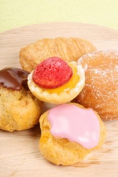 Assorted tea cakes on a wooden cutting board over a green background. With copyspace.