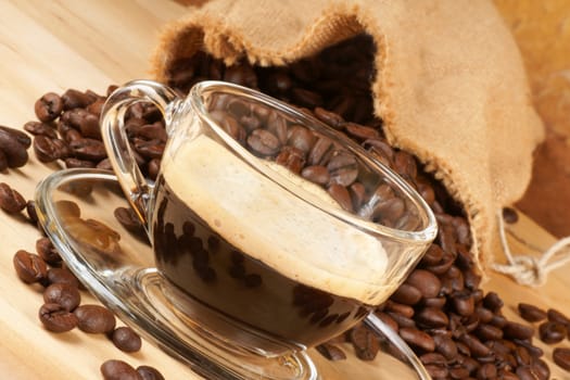 Close-up of a glass cup with italian espresso over a wooden table, surrounded by coffee beans.