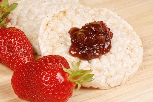 Close-up of two rice cakes with jam and some fresh strawberries on a wooden background for an healthy breakfast