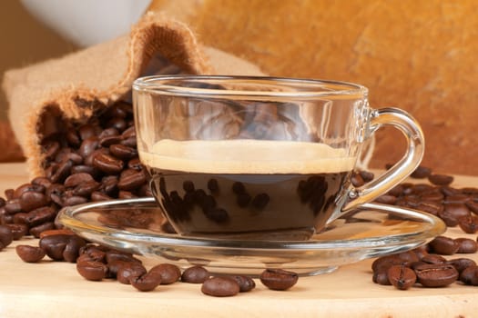 Close-up of a glass cup with italian espresso over a wooden table, surrounded by coffee beans.