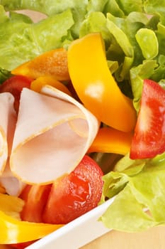 Close-up of a mixed salad with lettuce, tomatoes, bell peppers and roast turkey over a wooden cutting board