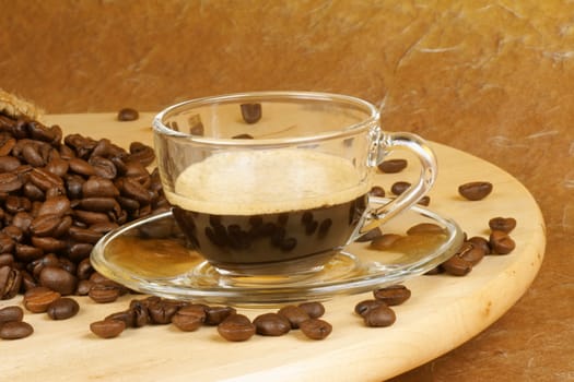 Close-up of a glass cup with italian espresso over a wooden table, surrounded by coffee beans.