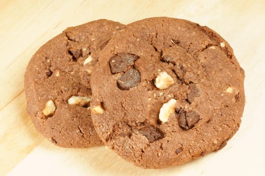 Two chocolate cookies with chocolate chips and hazelnuts over a wooden background