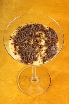 Vanilla custard cream with chocolate dessert served in a glass over an orange background. Selective focus.