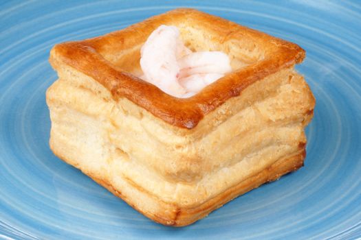 Close-up of a squared vol-au-vent stuffed with small boiled shrimps on a blue plate