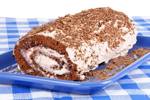 Chocolate swiss roll cake with berries marmalade and whipped cream served on a blue plate over a chequered background