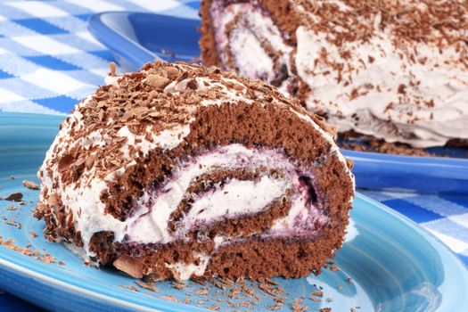 Chocolate swiss roll cake with berries marmalade and whipped cream over a chequered background