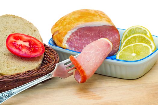 On a cutting Board is ham, bread, lemon and tomato. Presented on a white background.