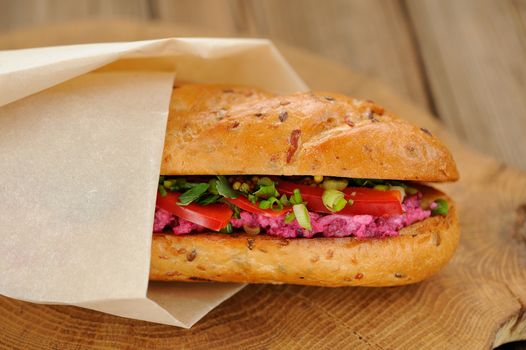 Sandwich with beetroot, bell pepper and scallion wrapped in paper horizontal closeup