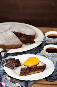 Chocolate cake with mango and black tea on blue cloth with space background vertical