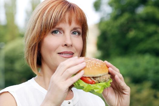 Portrait of an attractive woman who is eating a burger in a park