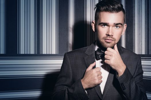 Portrait of a handsome man in a suit and a tie who is posing over a striped background