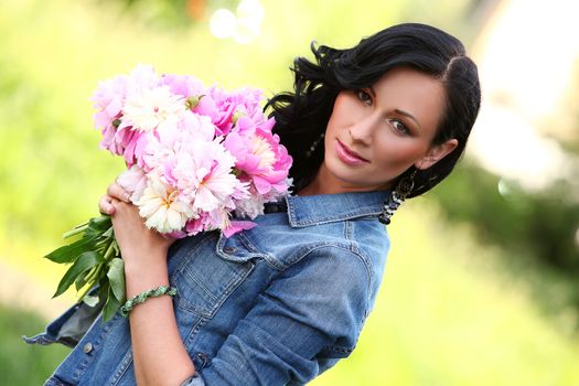 Beautiful caucasian woman in a park with bouquet of peonies