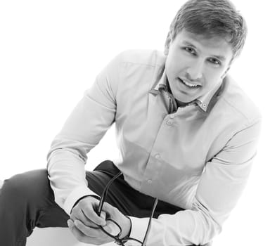 Handsome man in a shirt and trousers is sitting on a cube