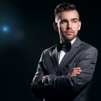 Portrait of a handsome man in a suit who is posing over a black background with a blue particles behind him