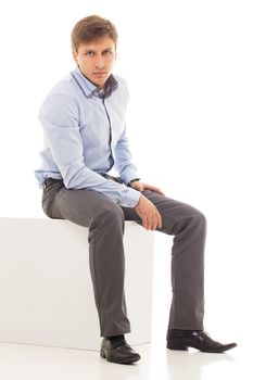 Handsome man in a shirt and trousers is sitting on a cube