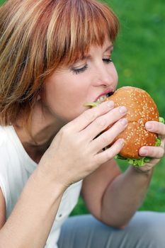Portrait of an attractive woman who is eating a burger in a park