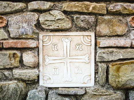 Ancient greek cross made of marble on the stone wall. Background