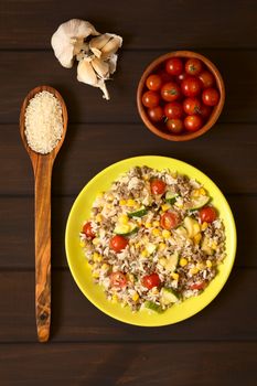 Overhead shot of rice dish with mincemeat and vegetables (sweet corn, cherry tomato, zucchini, onion) served on plate with ingredients around, photographed on dark wood with natural light