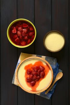 Overhead shot of semolina pudding with strawberry compote served in wooden bowl, photographed on dark wood with natural light  