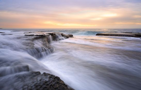 Fast flowing torrents at Curl Curl rock shelf.   One large waves flows off the rocks like a waterfall as the swell builds another wave.   These fast flowing waters feel like whitewater  river flows
