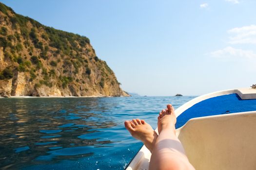 woman lounging on a catamaran sailboat trampoline with her feet propped up and crossed.  calm blue ocean and cloudless blue sky are in the background. copy space available