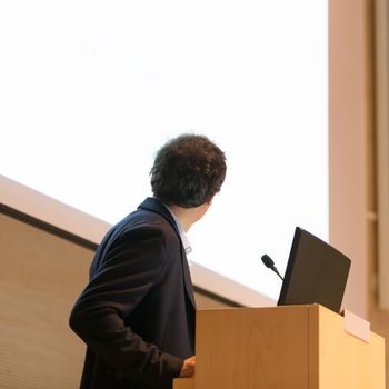 Speaker giving talk on podium at Business Conference. Business and Entrepreneurship. Expert presenting his work in lectures hall. Copy space.