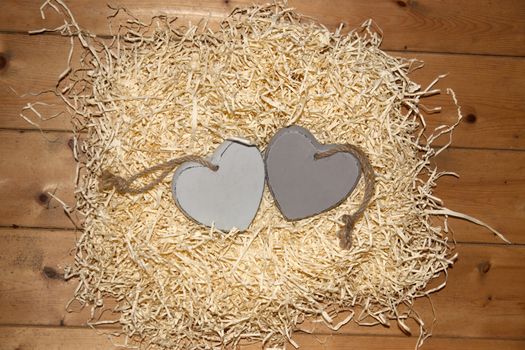 two blank grey wooden love hearts in a love nest made of straw with copy space