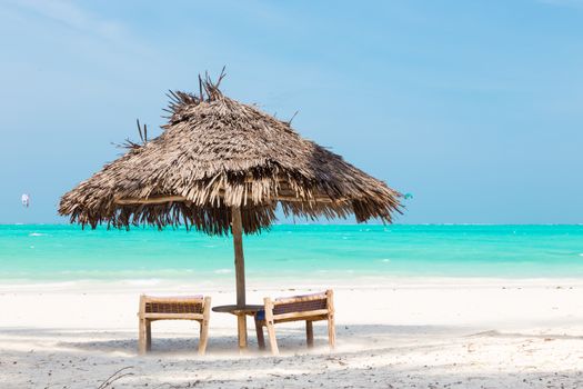 Two wooden dack chairs and umbrella on stunning tropical beach. Turquoise blue lagoon of Paje beach, Zanzibar, Tanzania.