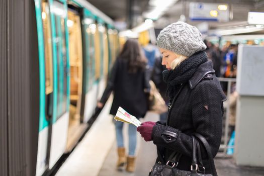 Casually dressed woman wearing winter coat, waiting on a platform for a train to arrive, orientating herself with public transport map. Urban transport.