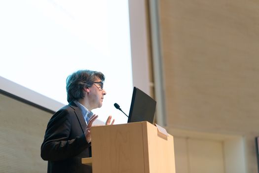 Speaker giving talk on podium at Business Conference. Business and Entrepreneurship. Expert presenting his work in lectures hall. Copy space.