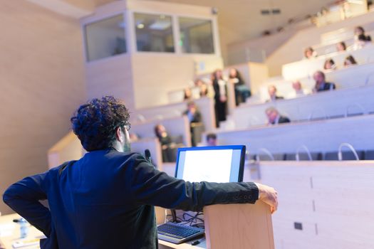 Speaker giving talk on podium at Business Conference. Business and Entrepreneurship. Expert presenting his work in lectures hall.