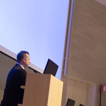 Speaker giving talk on podium at Business Conference. Business and Entrepreneurship. Expert presenting his work in lectures hall.