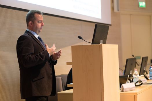 Speaker giving talk on podium at Business Conference. Business and Entrepreneurship. Expert presenting his work in lectures hall.