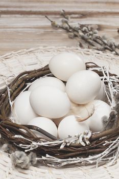 White eggs in nest on a brown wooden table. Done with vintage retro filter. Macro, selective focus