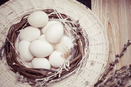 White eggs in nest on a brown wooden table. Done with vintage retro filter. Macro, selective focus