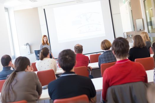 Speaker giving presentation in lecture hall at university. Participants listening to lecture and making notes. Copy space for brand on white screen.