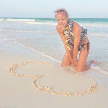 Beautiful woman drawing a heart in the sand on the beach.