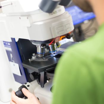 Male scientist microscoping on hi-tec fluorescent microscope. 