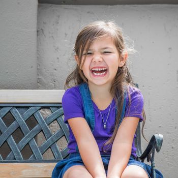 Little girl sits laughing on outside bench.