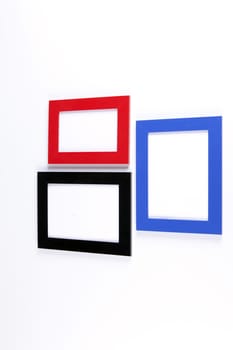 Three retro wooden photo frames, red, blue, black on white wall background.