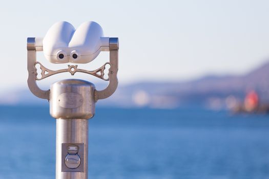 Telescope on a beach pointed at blue sea.